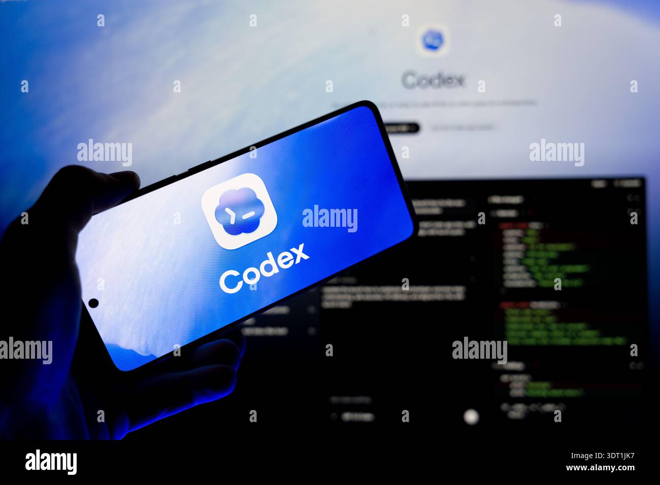 Hand holding smartphone displaying Codex AI logo on screen with blurred code editor background, concept for artificial intelligence in software develo Stock Photo