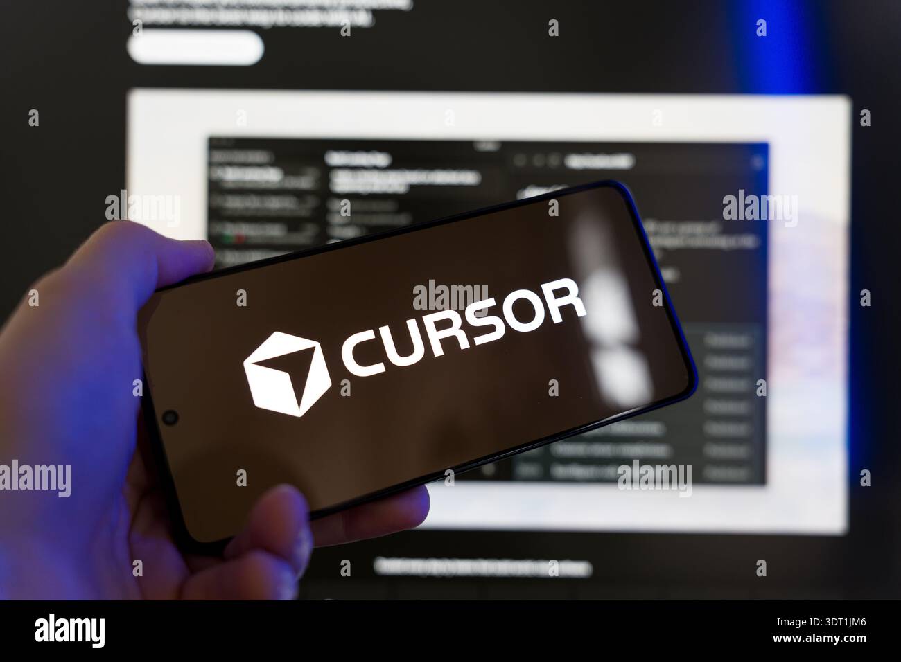 Hand holding smartphone displaying Cursor AI logo on screen with a blurred code editor in the background, artificial intelligence coding assistant and Stock Photo