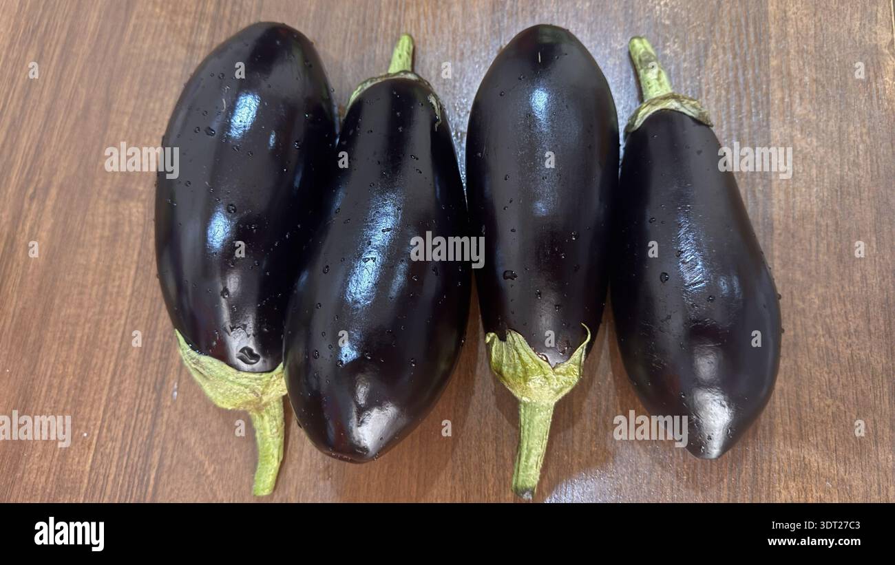 Fresh Whole Eggplants with Dew Drops on Wooden Surface Stock Photo