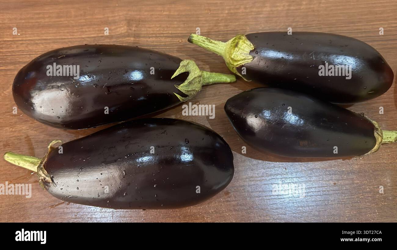 Fresh Whole Eggplants with Dew Drops on Wooden Surface Stock Photo