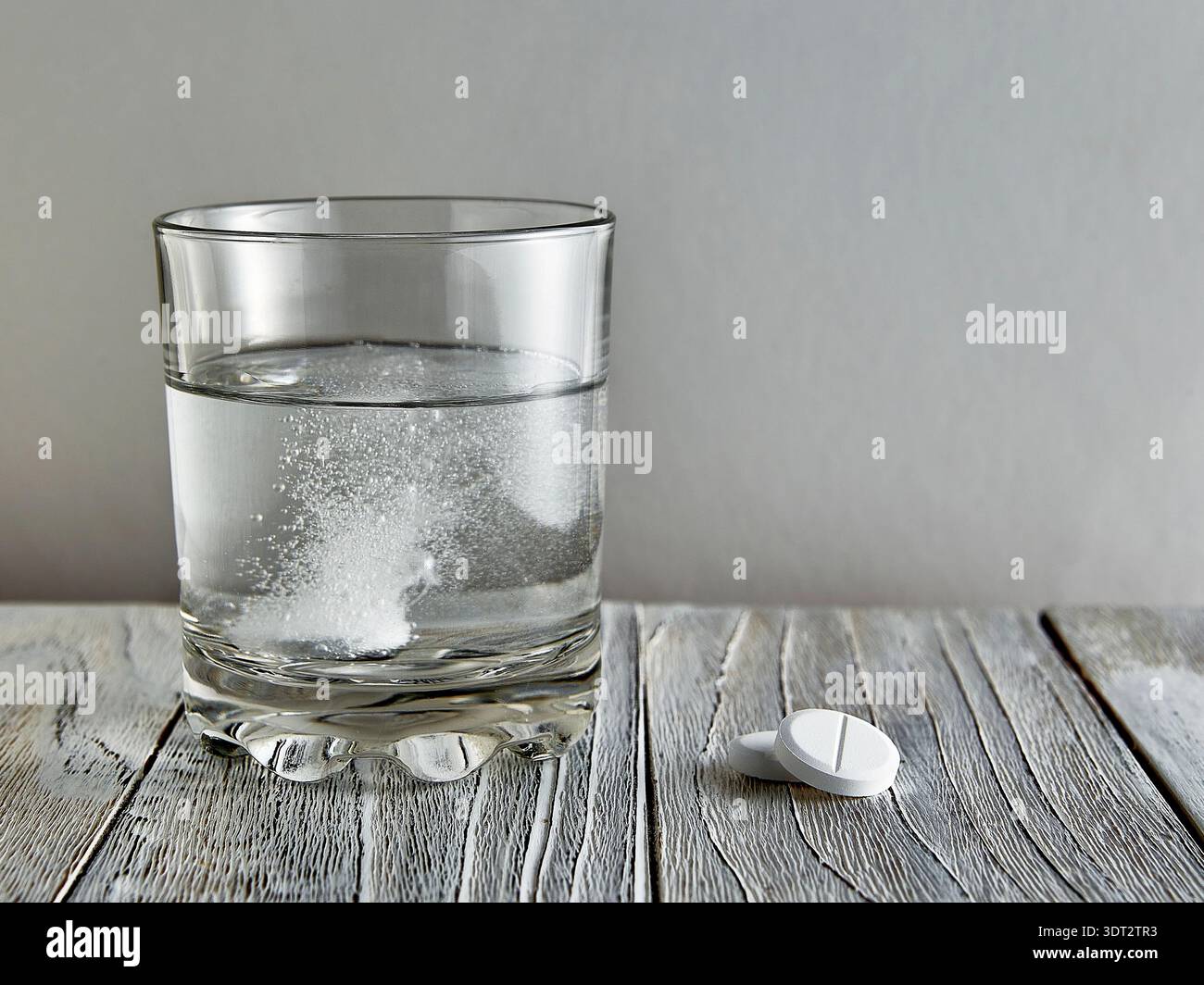 Effervescent tablet in a glass, next to two more tablets on a wooden table Stock Photo