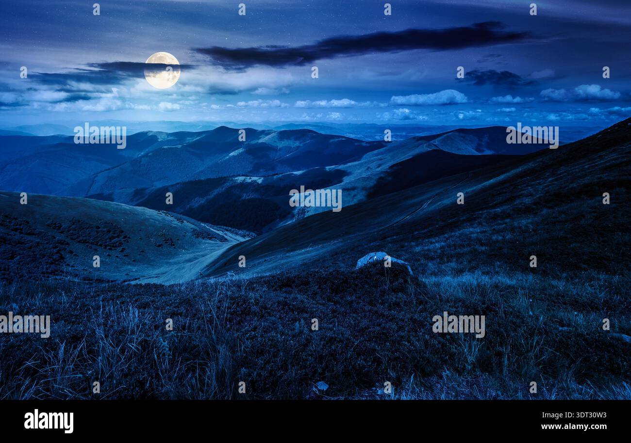 wonderful mountain landscape during summer night. stone among the grassy alpine meadow near the edge of a slope in full moon light. mysterious highlan Stock Photo