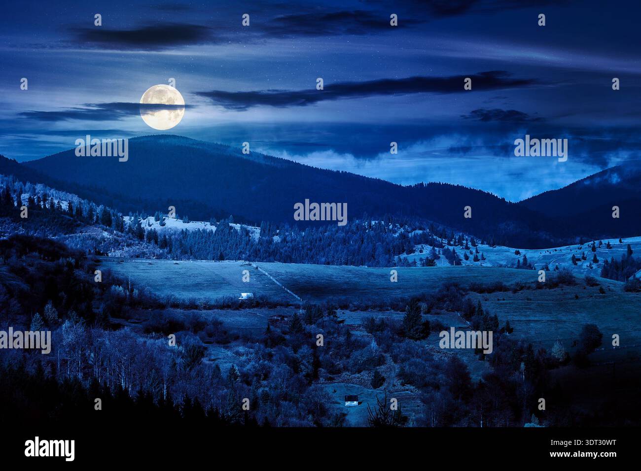 autumn landscape of rural region in mountains at night. rolling hills with green alps in dappled full moon light. serene countryside under cloudy sky. Stock Photo