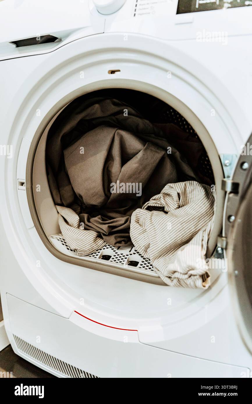 Open washing machine with a load of clothes inside the drum in a home interior Stock Photo