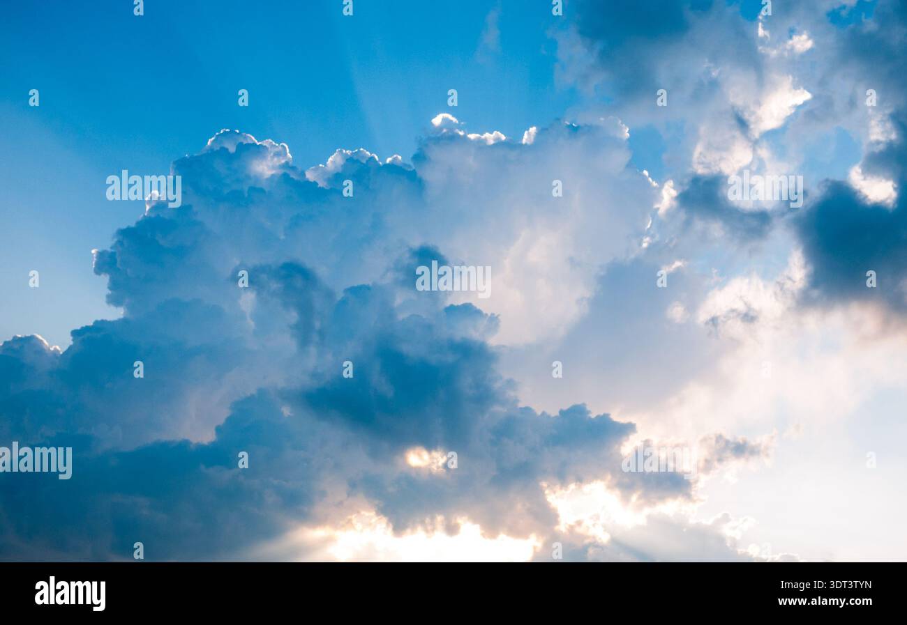 Dramatic clouds with sun rays breaking through blue sky Stock Photo