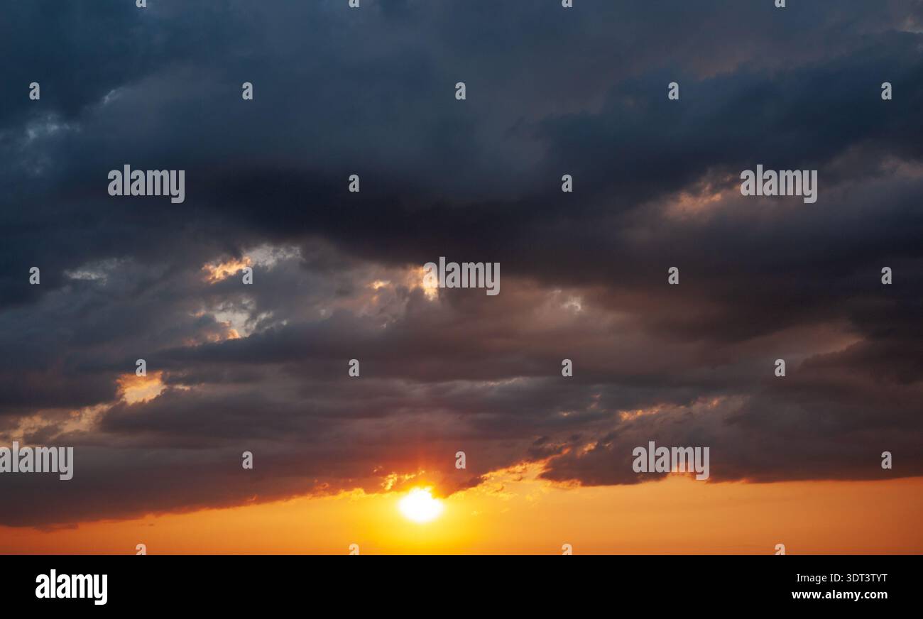 Dramatic dark clouds with sun rays breaking through sunset storm sky Stock Photo