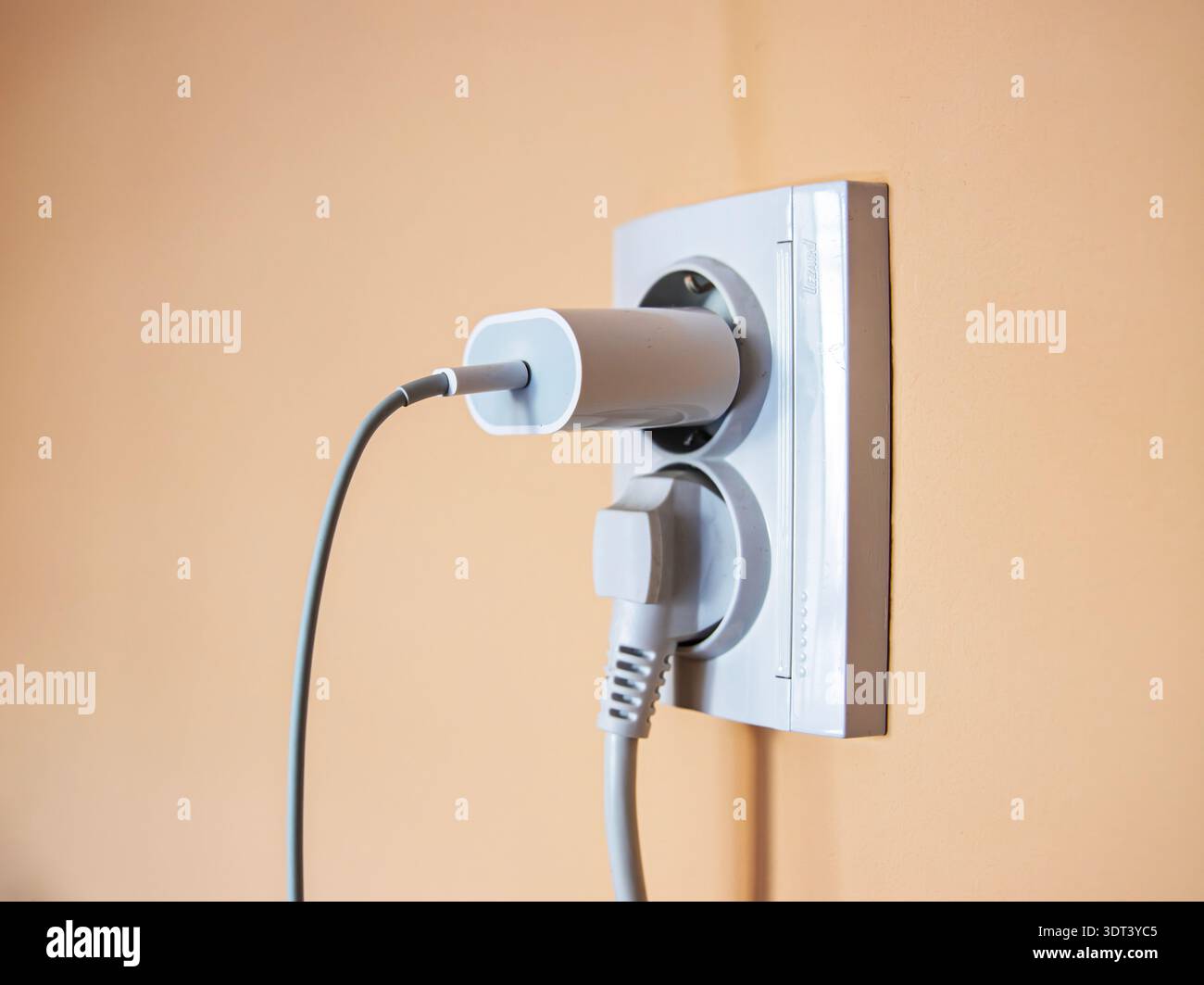 White wall socket with connected power adapter and thick cord in residential interior setting Stock Photo