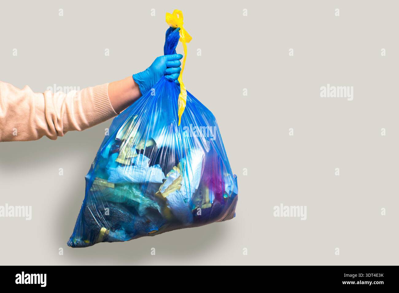 Hand holding full garbage bag on grey background isolated. High quality image Stock Photo