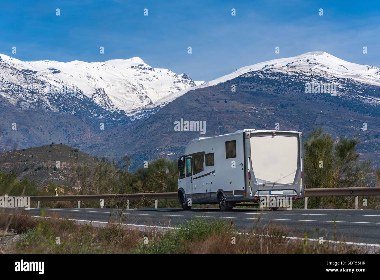 Motorhome driving on a mountain road with snowy mountains in the background Stock Photo