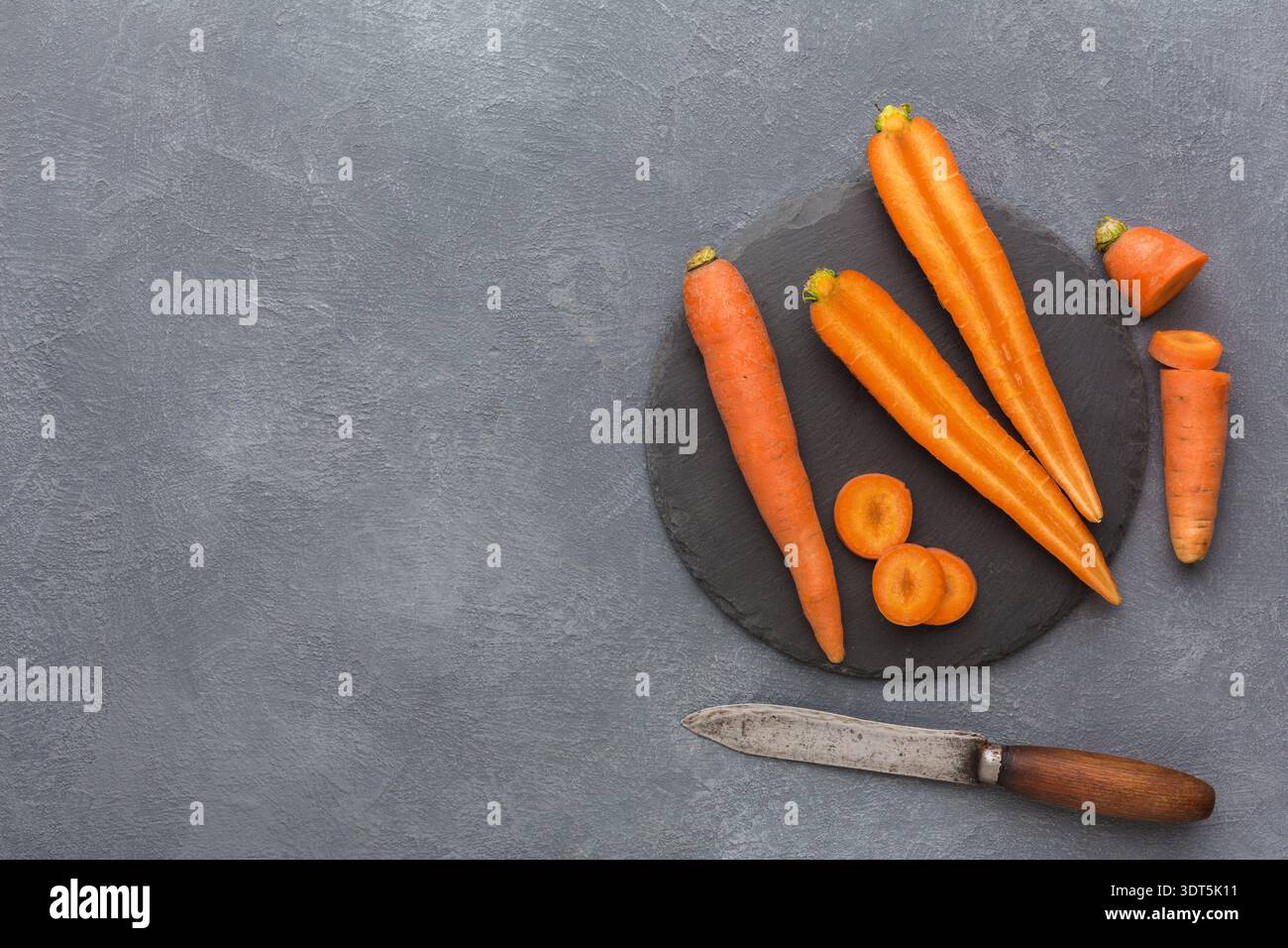Fresh Carrots Arranged on a Dark Plate With a Knife for Cooking or Preparation on a Gray Surface Stock Photo