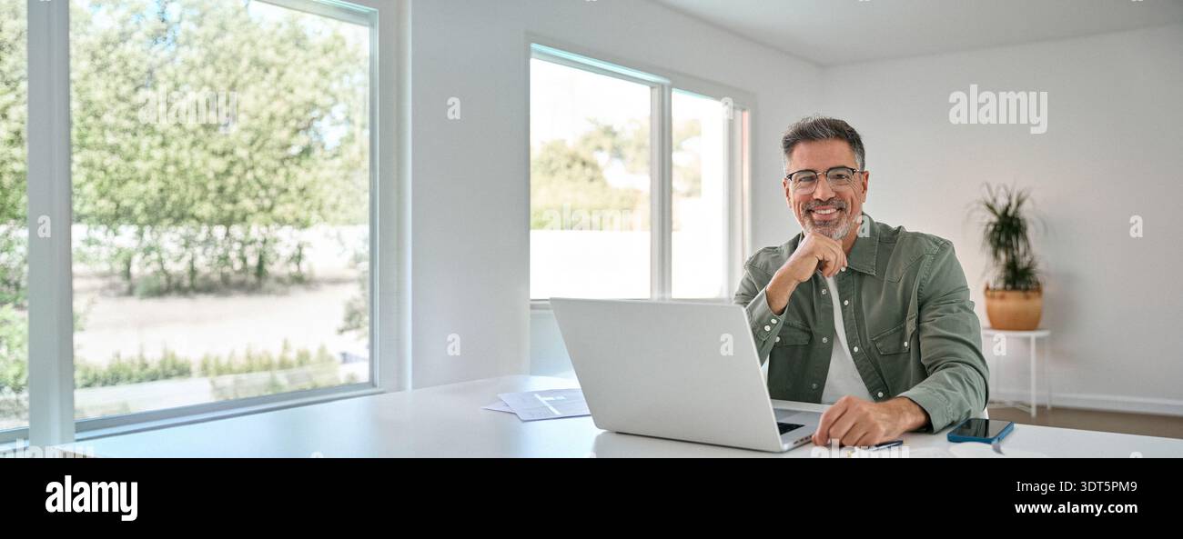 Happy older middle aged man using laptop computer at home table. Portrait Stock Photo