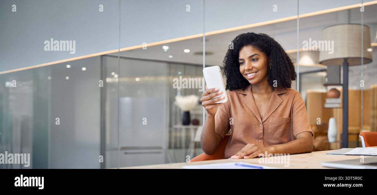 Young happy African American business woman using cell phone sitting in office. Stock Photo