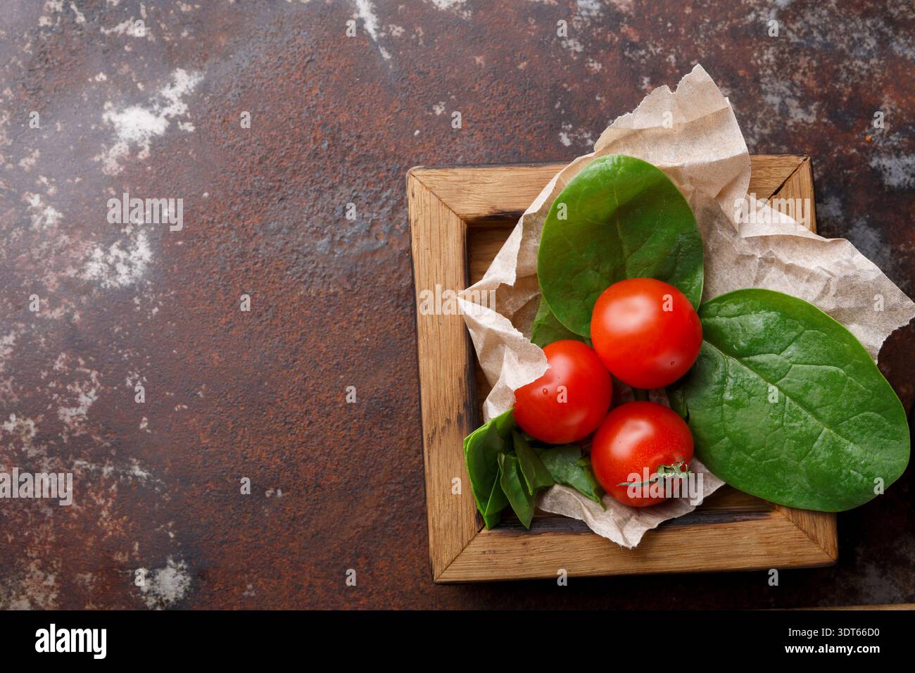 Fresh Tomatoes and Spinach on Brown Surface in a Wooden Plate Stock Photo