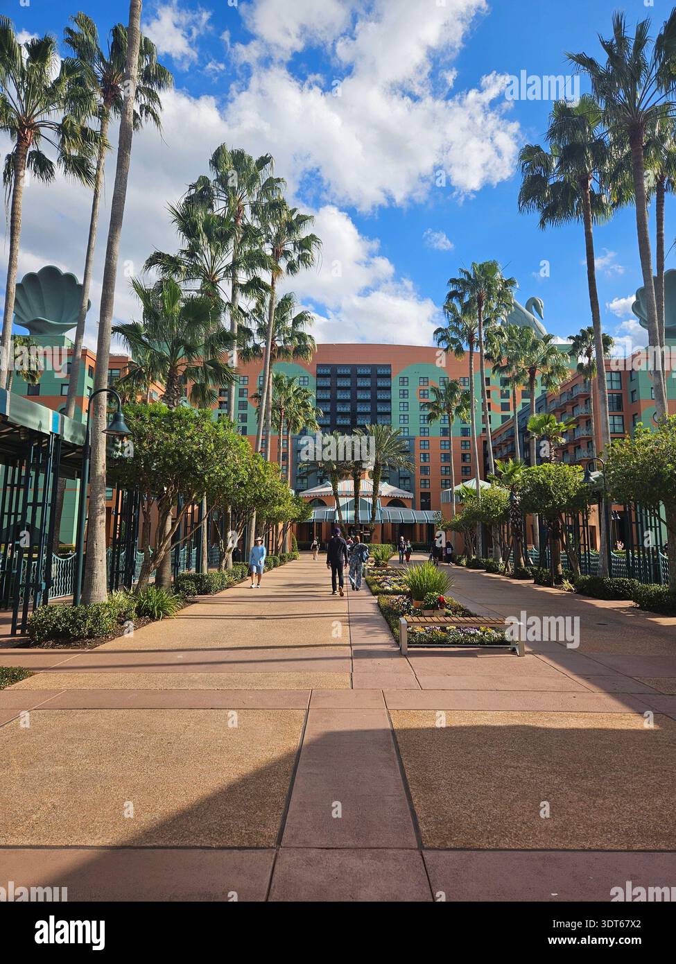 EDITORIAL USE ONLY-  ​LAKE BUENA VISTA, FLORIDA - JANUARY 2026: An outdoor view of the Walt Disney World Swan Hotel, featuring its iconic "entertainment architecture" designed by Michael Graves. The coral-and-aqua facade is crowned with massive 47-foot-tall swan statues and giant decorative clamshells. Palm trees and a landscaped walkway lead guests toward the 12-story main building and its distinctive gently arching rooftop. - Smartphone Captured Stock Image