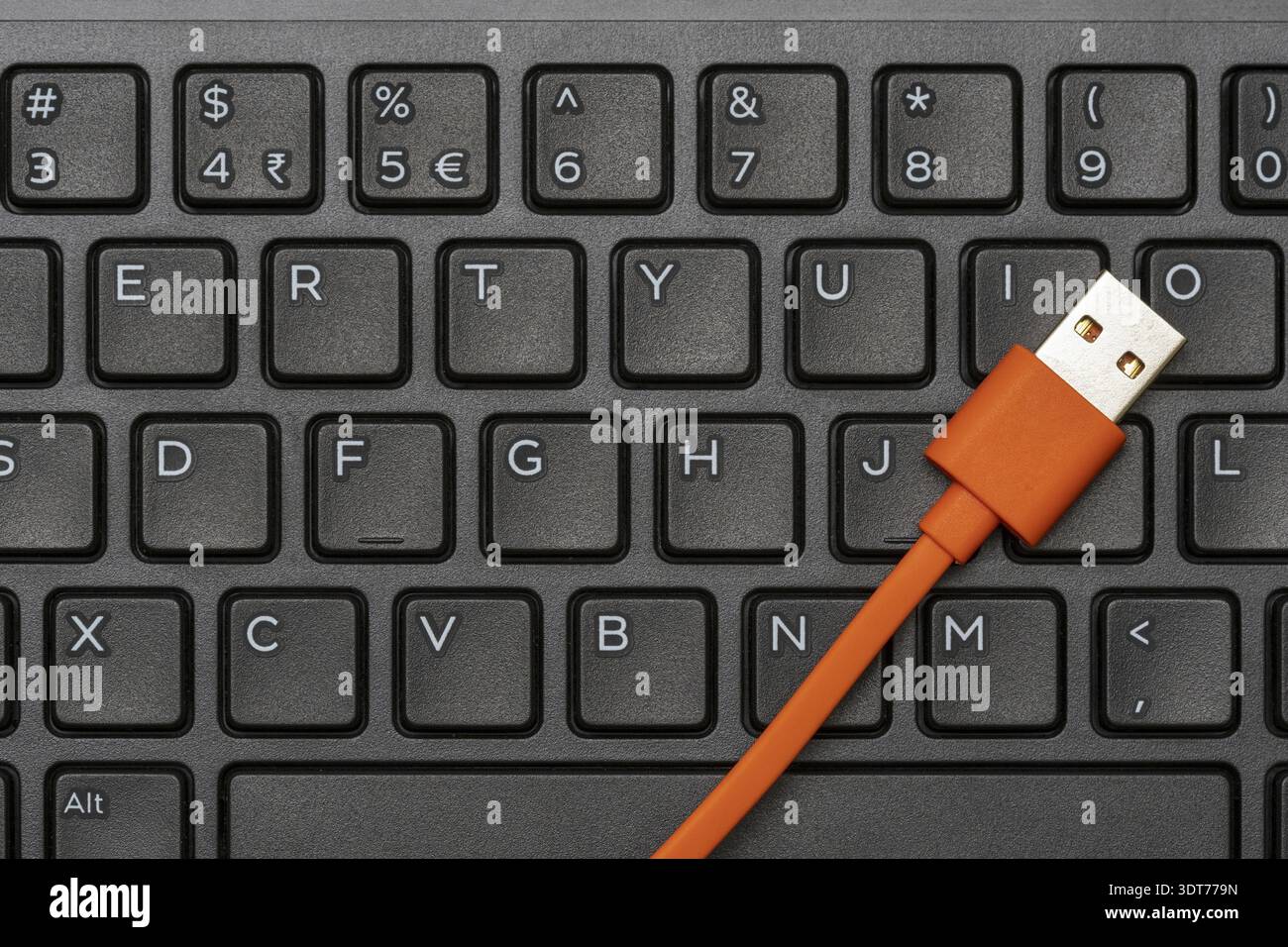 Computer keyboard and orange USB cable for charging peripheral or data transfer Stock Photo