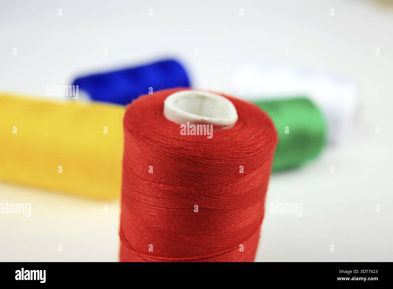Red spool of thread in focus with other colorful rolls in the background Stock Photo