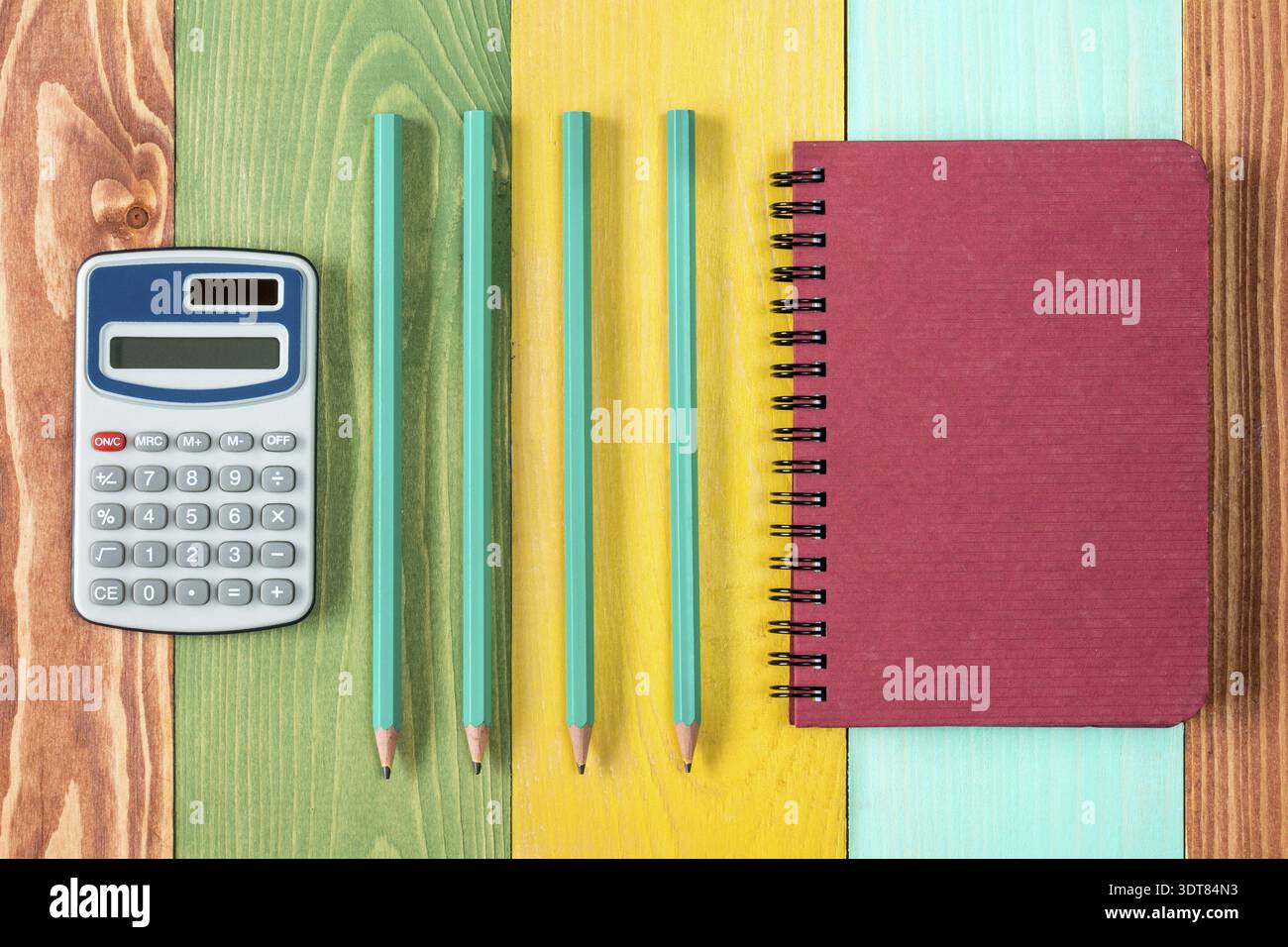 Notebook, calculator and four pencils on colored background Stock Photo