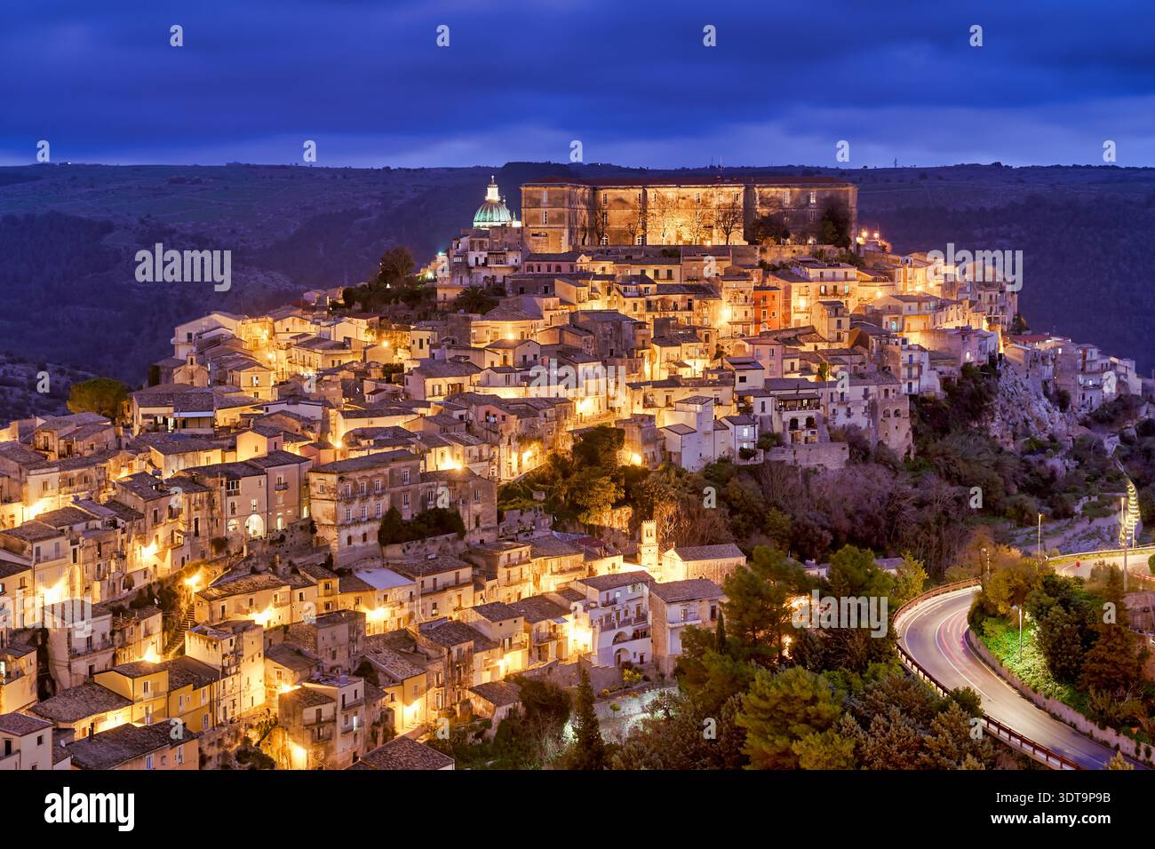 Ragusa Ibla shows its charm during sunset with warm lights emerging from the buildings. The skyline reflects the beauty of the old town. Stock Photo