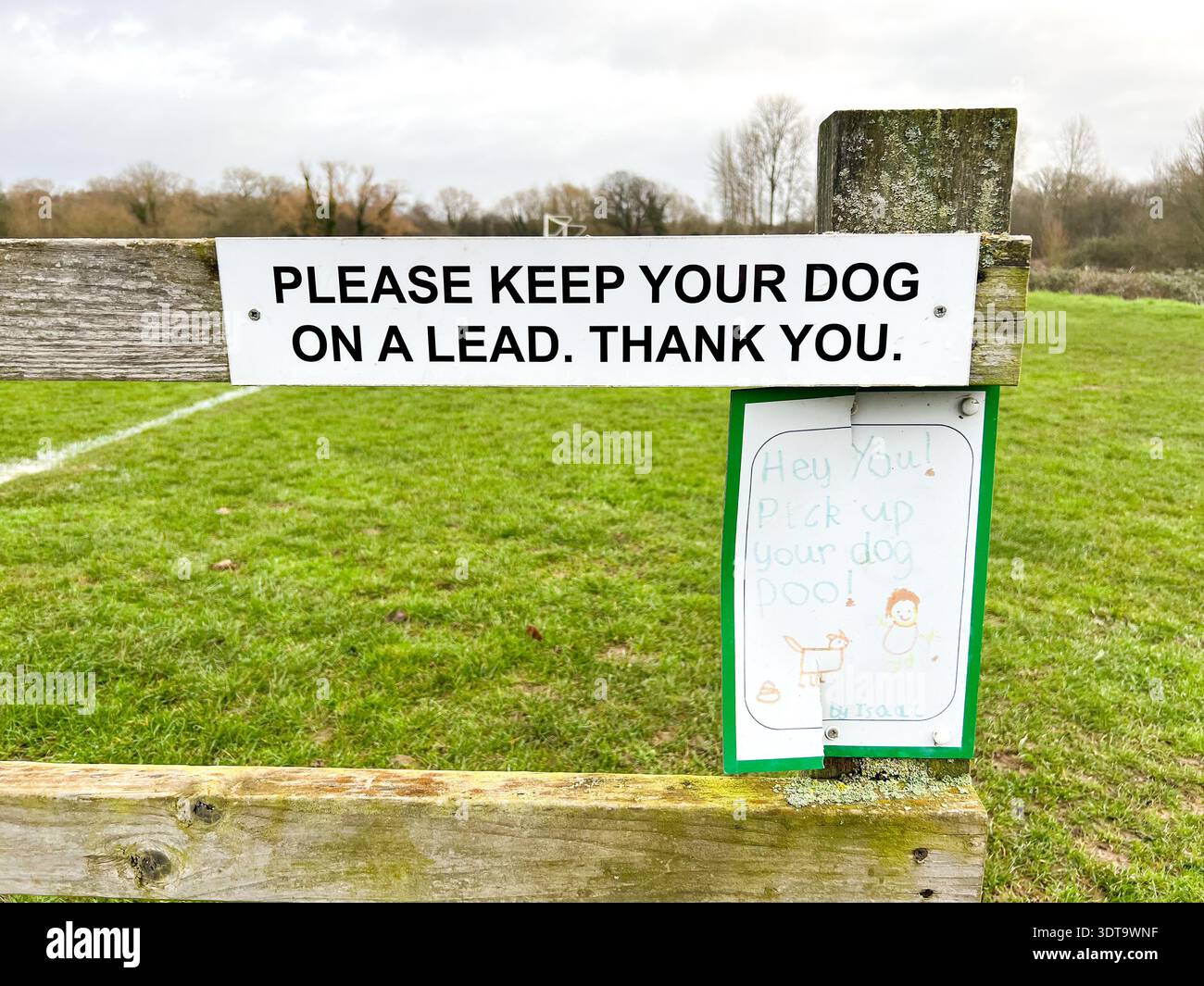Signs attached to a wooden fence at the entrance of a public park ask dog owners to keep dogs on leads and pick up any dog poo - Smartphone Captured Stock Image