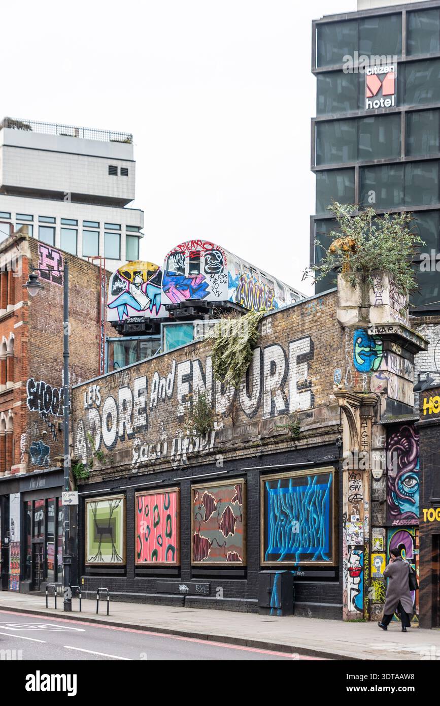 Street art graffiti on Great Eastern Street, Shoreditch, including two old underground trains above street. Let's adore & endure each other slogan Stock Photo