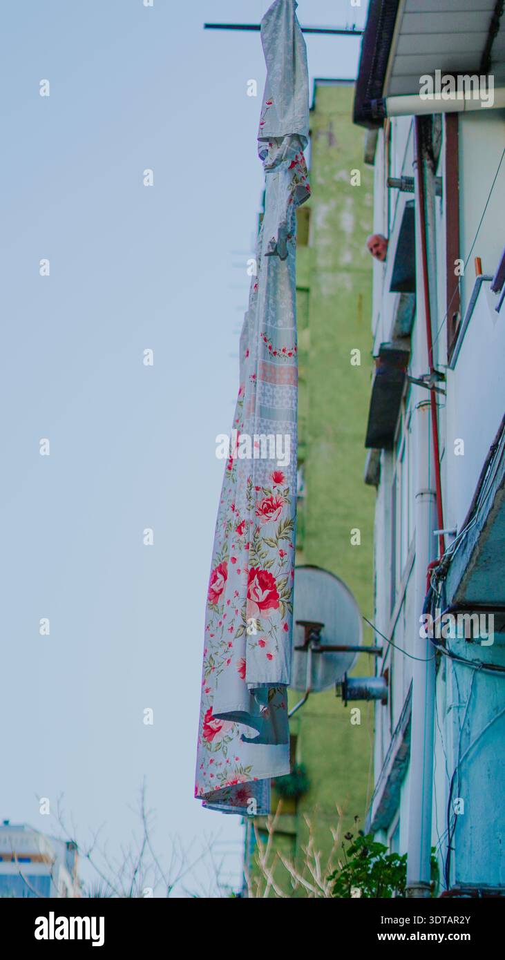 A floral-patterned curtain is draped outside a building in an urban environment under clear skies Stock Photo