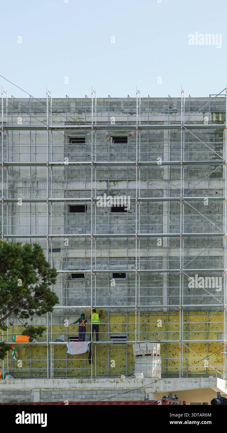 Two construction workers in safety gear work on scaffolding at a ...