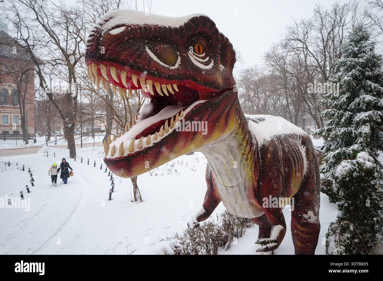 a-woman-walks-with-a-child-past-an-animated-model-of-a-dinosaur-outside