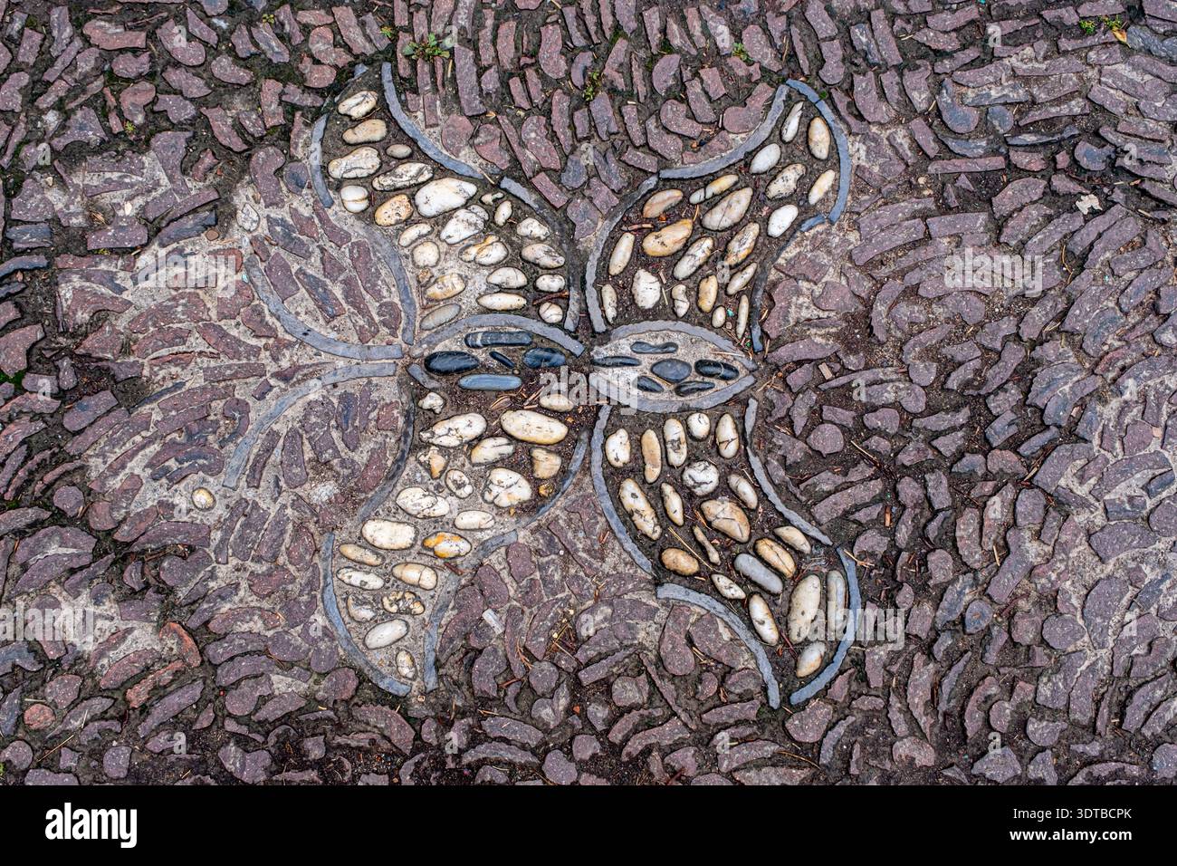 a cobblestone pavement featuring an intricate, symmetrical pattern with alternating dark and light stones forming a geometric design. Stock Photo