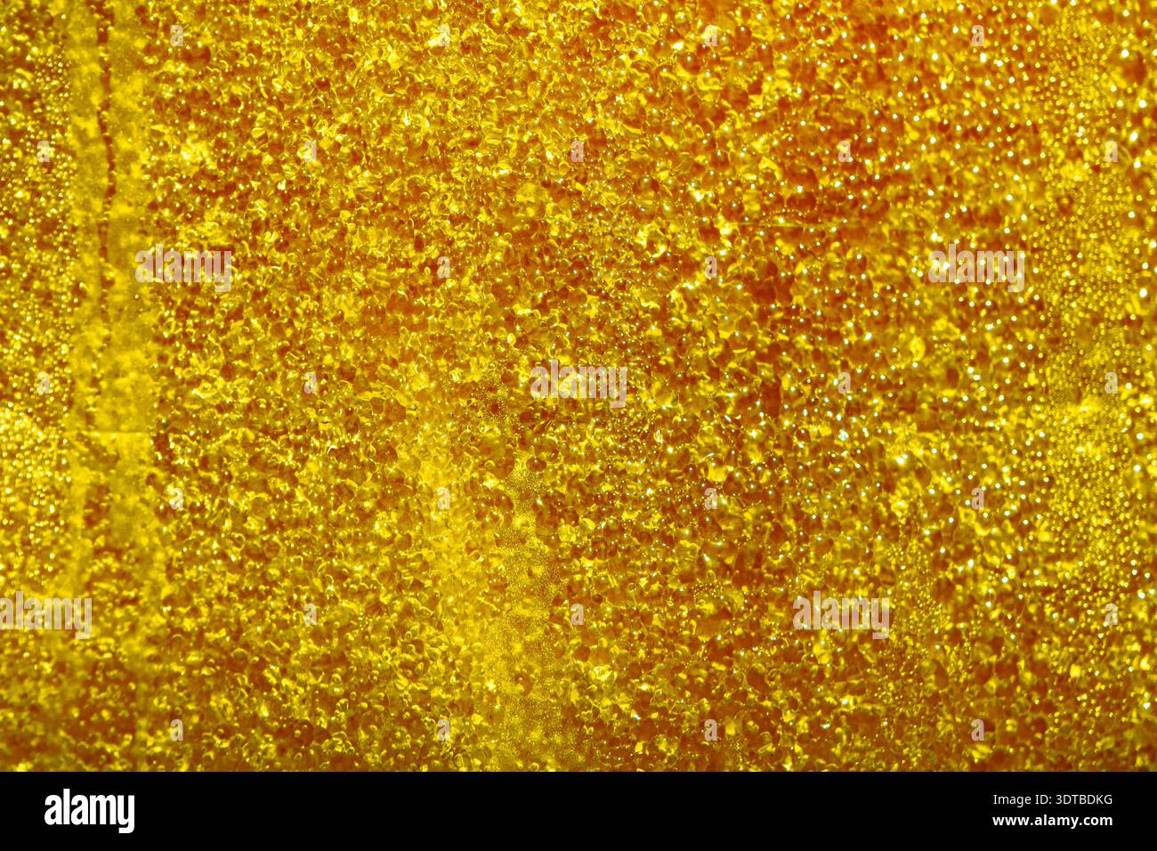 a vibrant golden surface covered in numerous small water droplets. The red background is slightly textured, creating a subtle gradient effect. Stock Photo