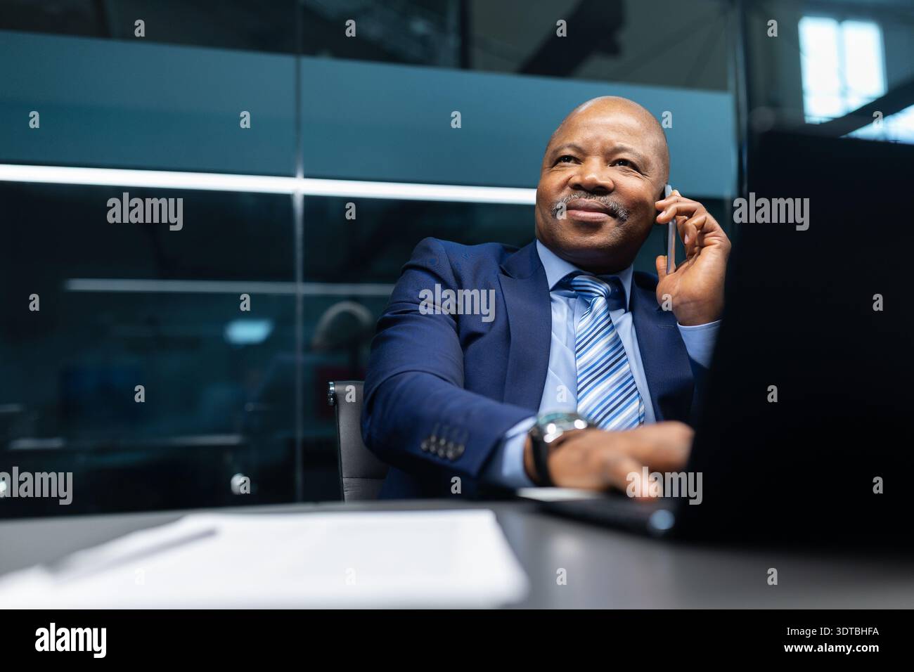 Confident mature black businessman talking on smartphone at desk in modern office Stock Photo