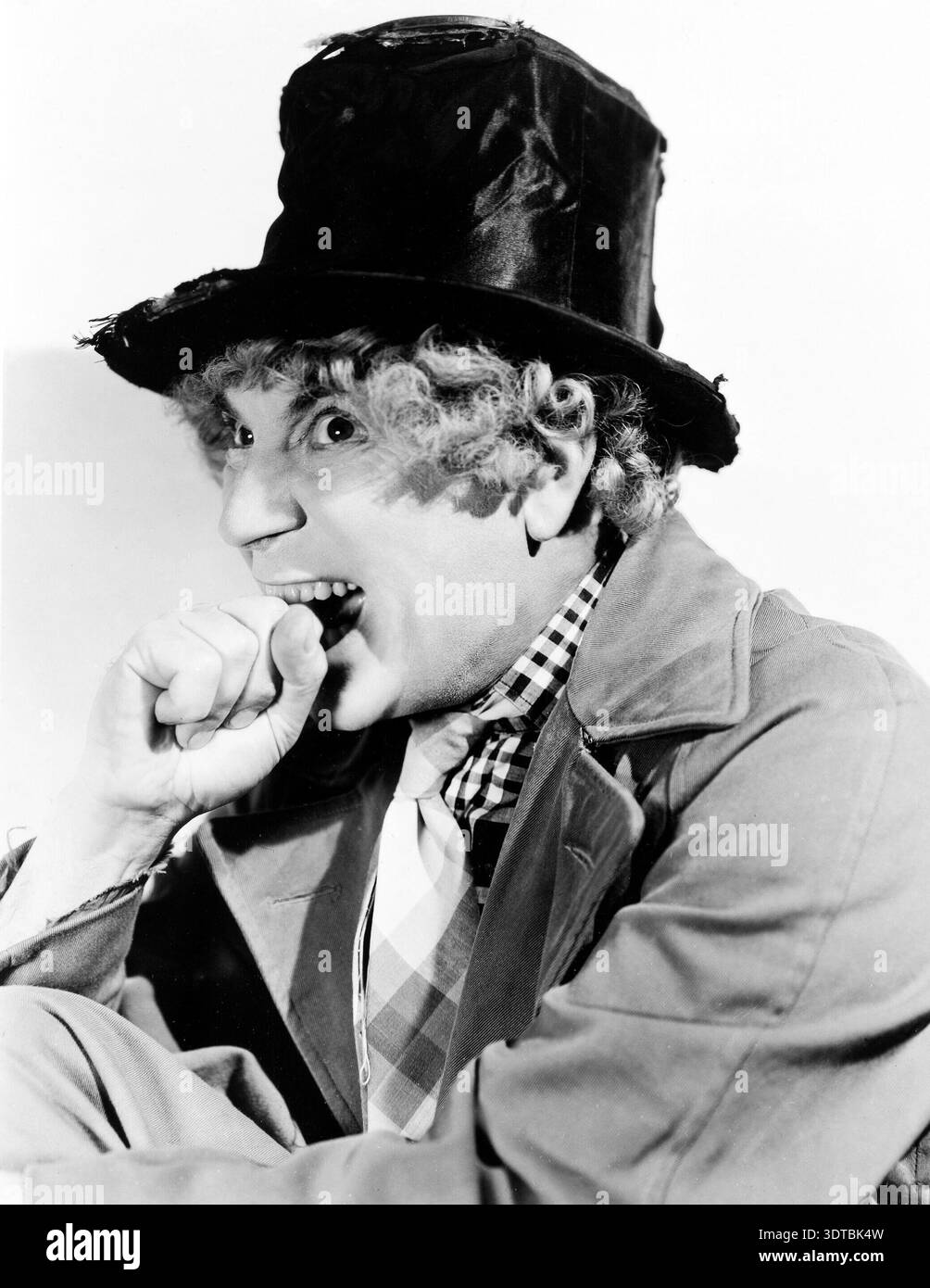 A striking black and white portrait from the 1930s of Harpo Marx, an American comedian, actor, and musician, known for his silent visual gags as part of the Marx Brothers. He is depicted in character with a tattered top hat, curly wig, and an open-mouthed expression, biting his fist. Stock Photo