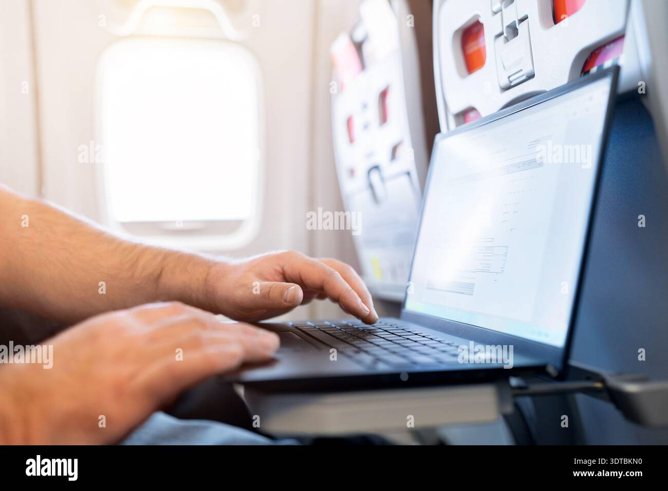 Adult caucasian male traveler working on laptop by airplane window Stock Photo