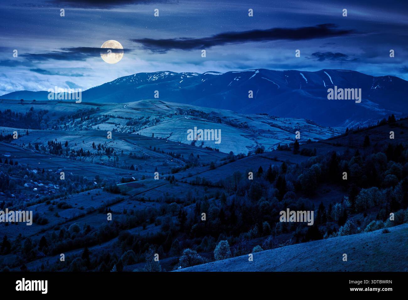 rural landscape in spring at night. full moon over rolling countryside scenery with wooded hills. lovely view to the valley. high mountain range in th Stock Photo