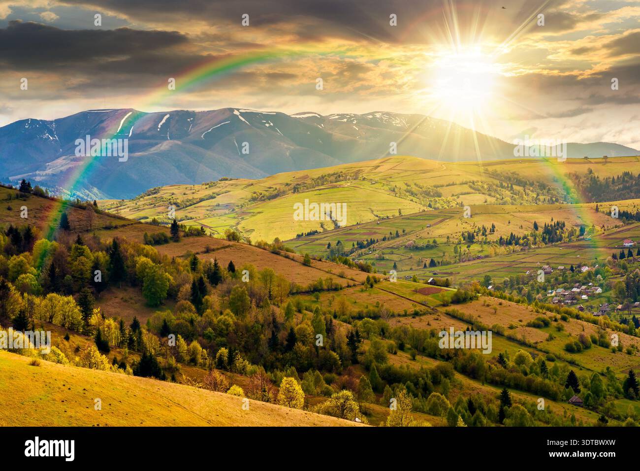 sunset over rural landscape in spring. rolling countryside scenery with wooded hills. lovely view to the valley. high mountain range in the background Stock Photo