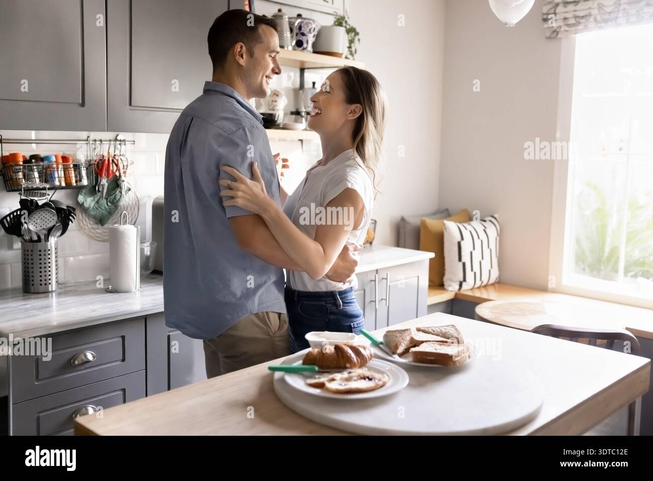 Couple embracing and laughing during romantic morning in kitchen Stock Photo