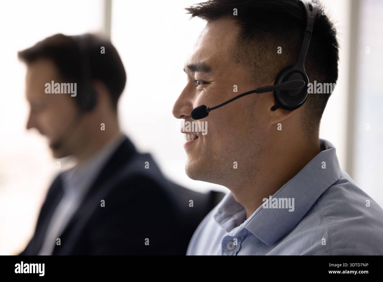 Smiling young man hotline operator in headphones receiving phone call Stock Photo