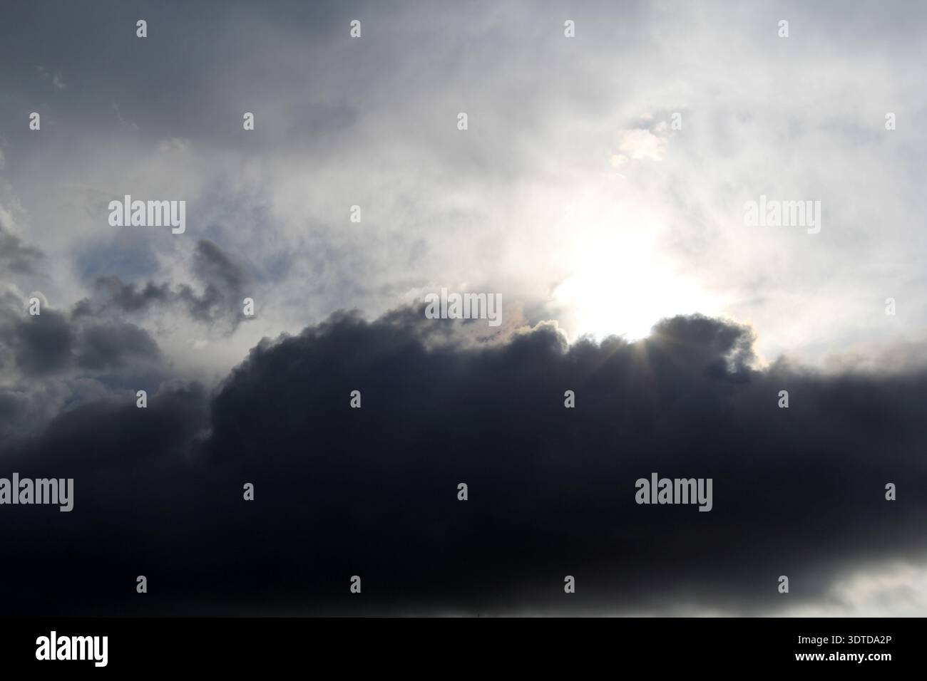 Sun partially hidden behind a dark cloud in a dramatic sky Stock Photo