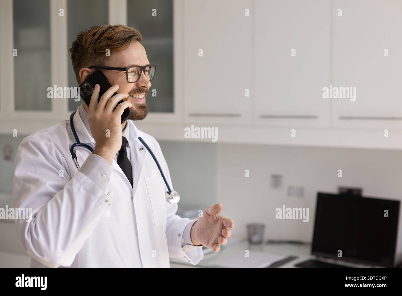 Smiling young male physician holding phone conversation from clinic office Stock Photo