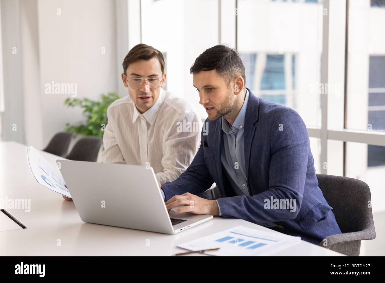 Two focused young businessmen sitting at conference desk using laptop Stock Photo