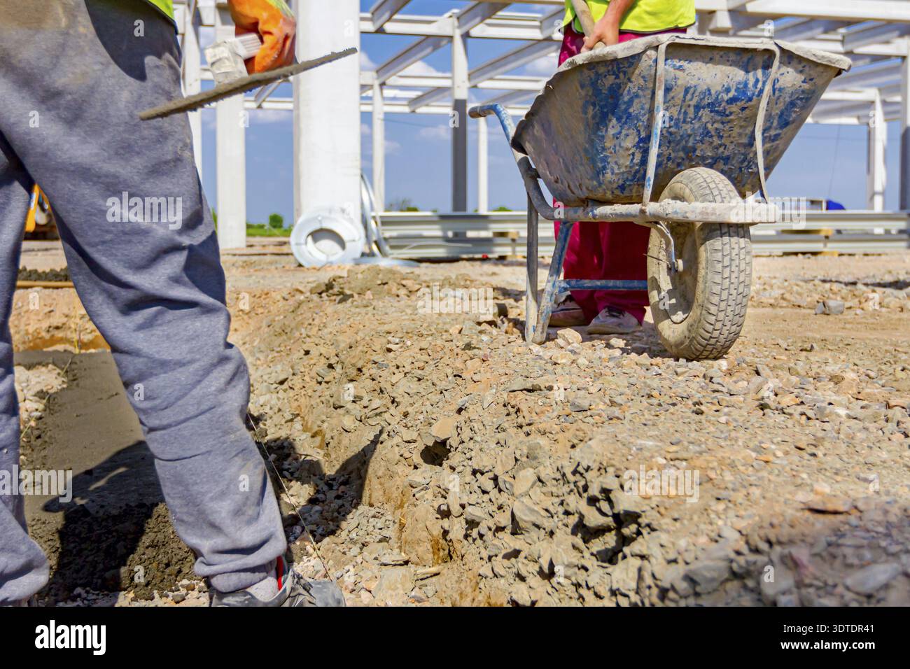 Construction worker is using shovel to unloading cement from wheelbarrow on construction site Stock Photo