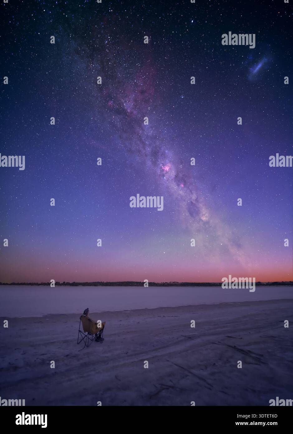A person (the photographer) sits and watches the Milky Way rise above a dried out salt lake in the Wheatbelt of Western Australia. Stock Photo