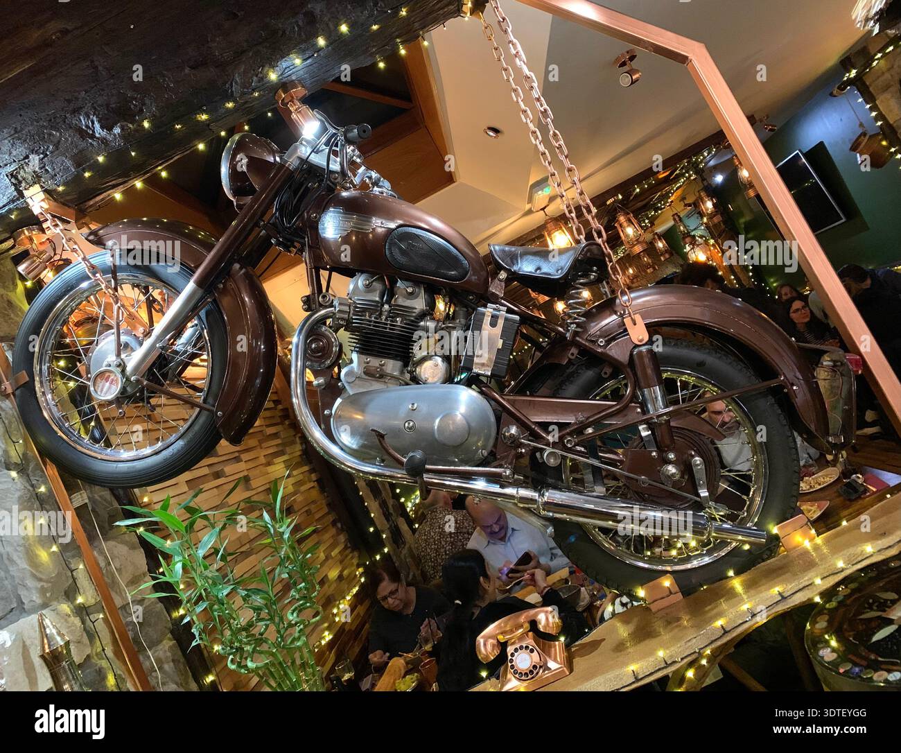 Vintage motorbike suspended as quirky decor in a lively warmly lit restaurant in Leicester adding retro character above the busy tables below - Smartphone Captured Stock Image