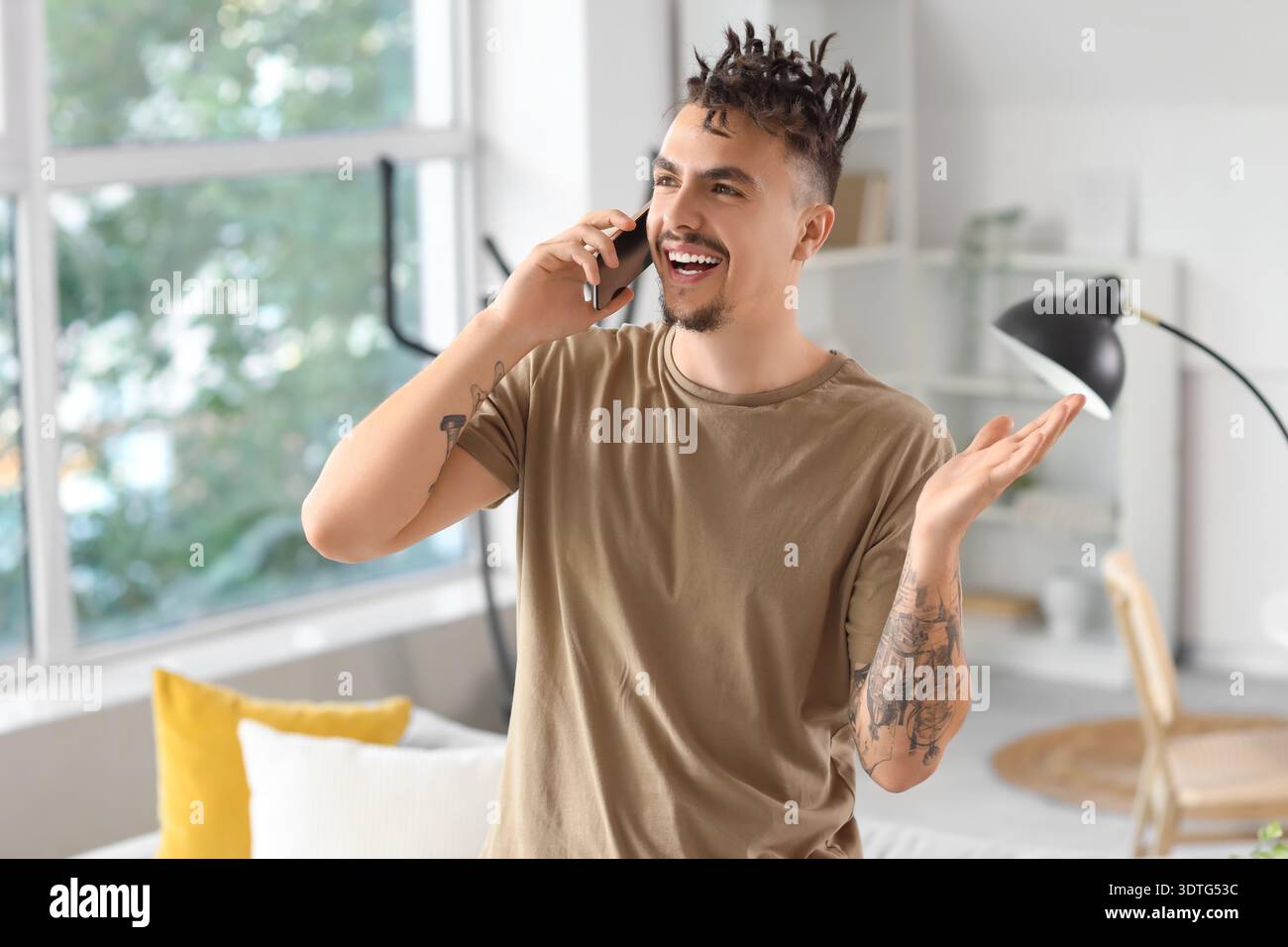 Young man with dreadlocks talking by mobile phone at home Stock Photo