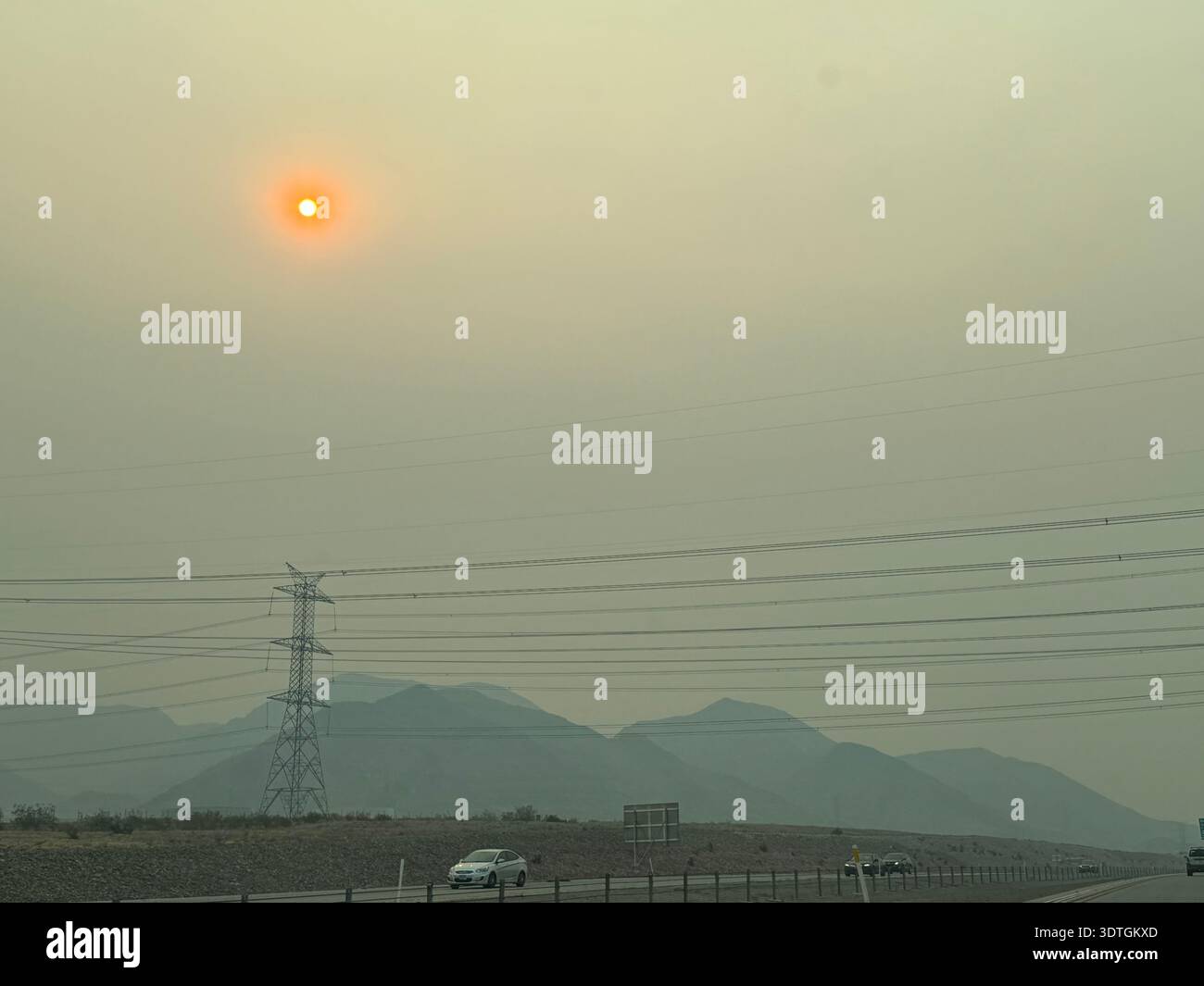 Hazy sun over desert highway with electricity transmission lines and mountains in the background in the American Southwest, Nevada, USA. - Smartphone Captured Stock Image