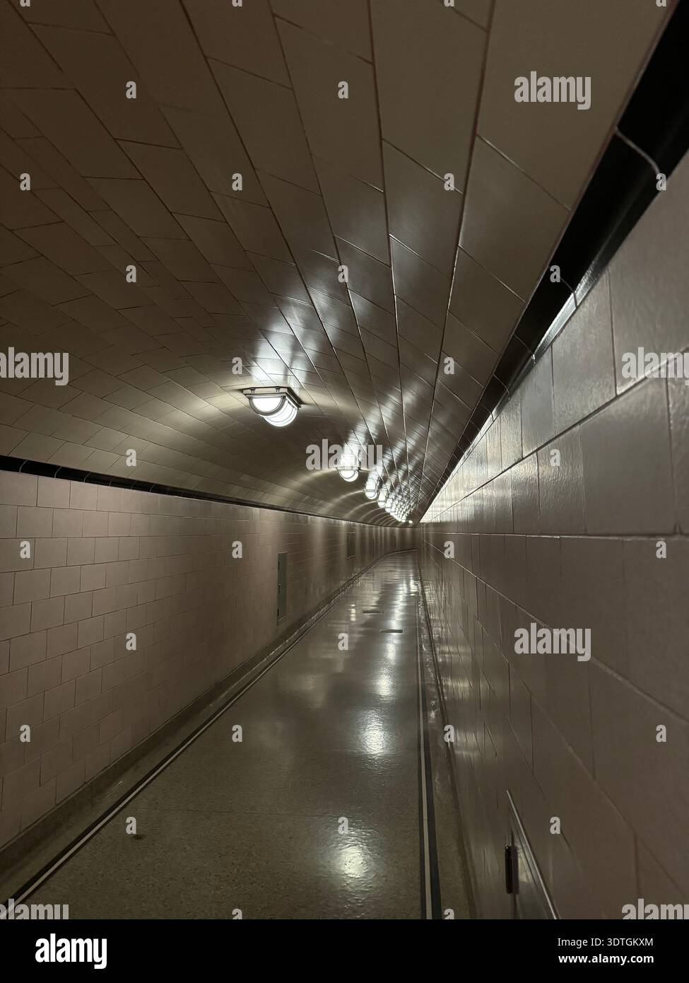 Long illuminated pedestrian tunnel corridor with tiled walls and ceiling lights creating strong perspective lines in an underground passage. - Smartphone Captured Stock Image