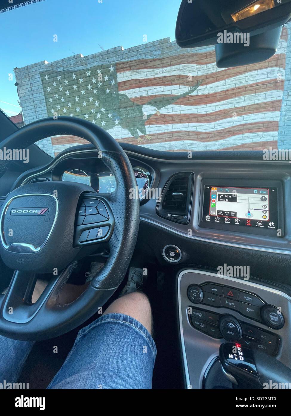 View from inside a Dodge car with steering wheel and dashboard, parked in front of a wall mural of the American flag with eagle silhouette, USA. - Smartphone Captured Stock Image