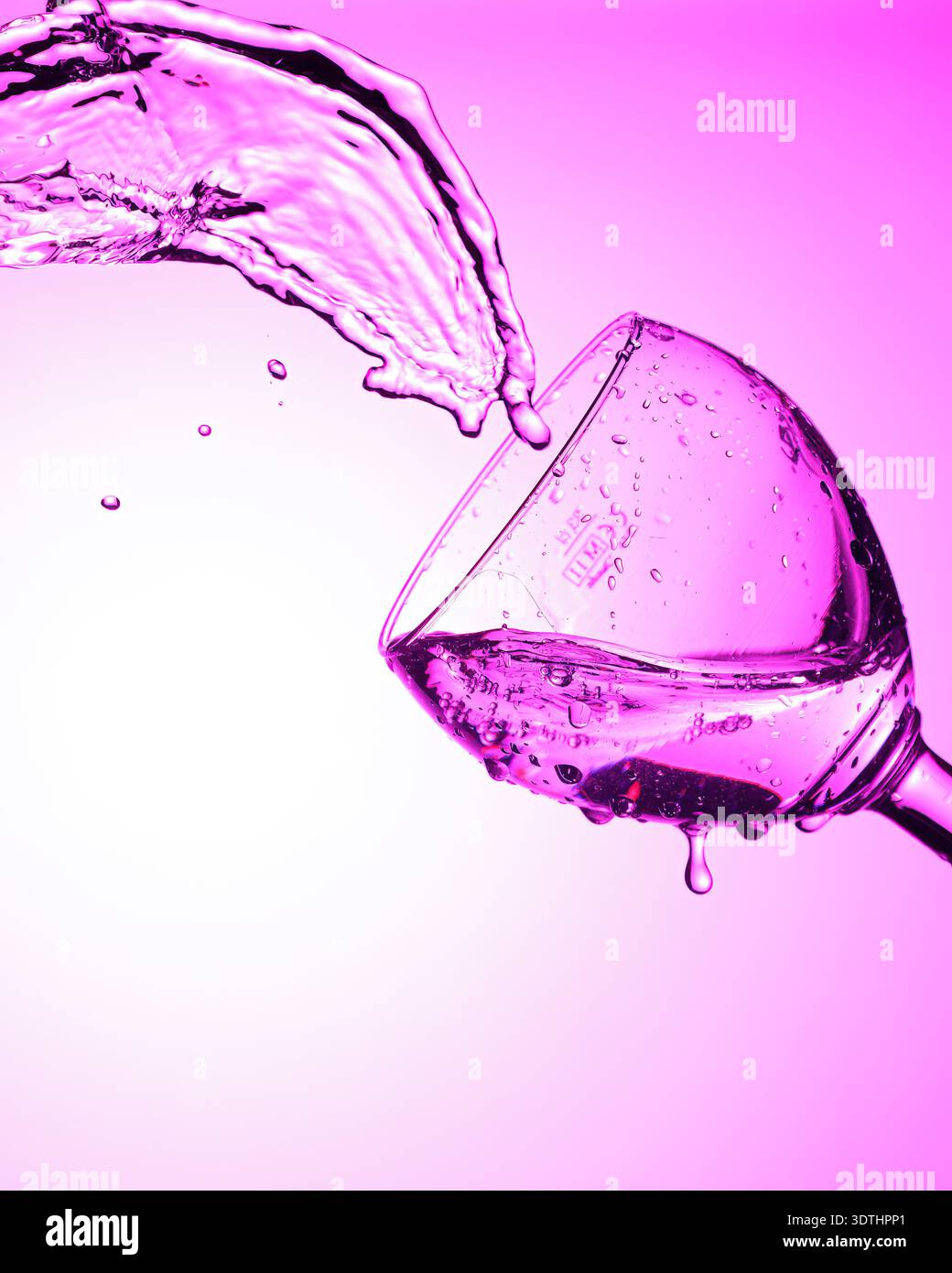 Liquid splashes from tilted glass with purple lighting. Stock Photo
