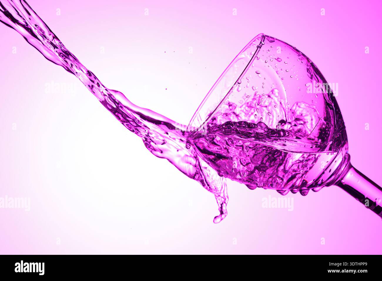 Liquid splashes from tilted glass with purple lighting. Stock Photo