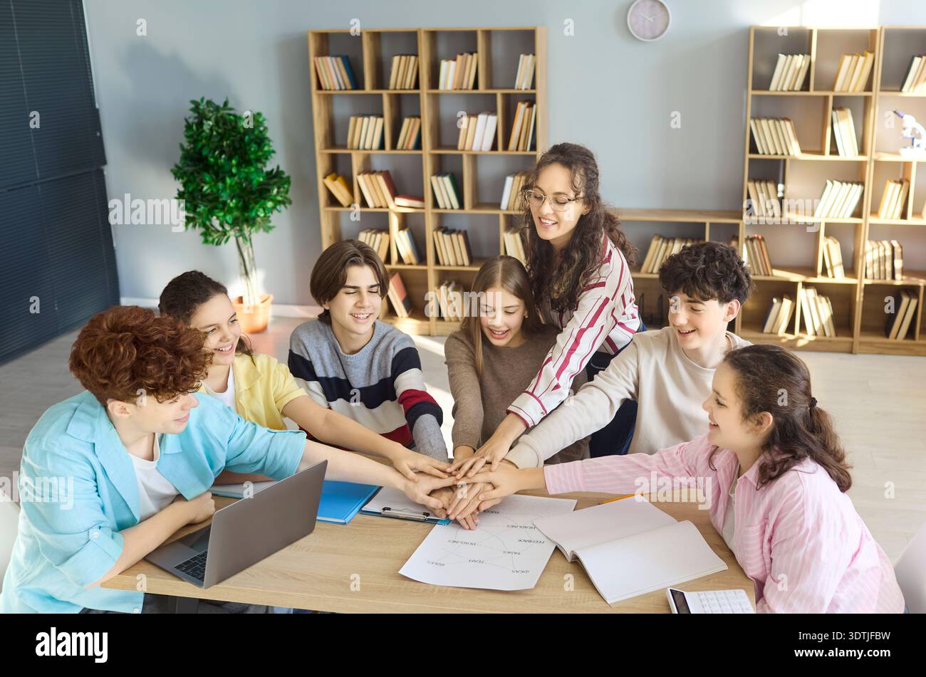 Happy teen students stacking hands during teamwork in library study group Stock Photo