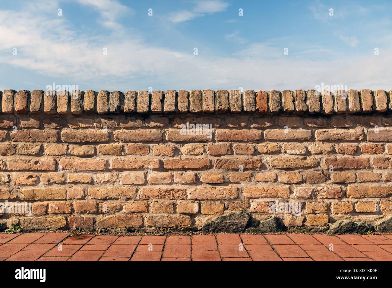 Old brick wall with terracotta coping and blue sky background, selective focus Stock Photo